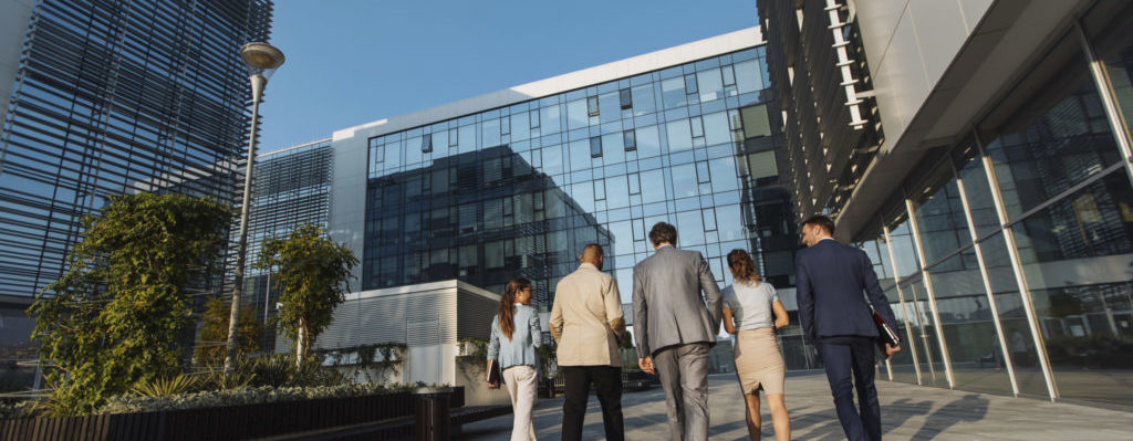 Back shot of five businesspeople walking next to an office building