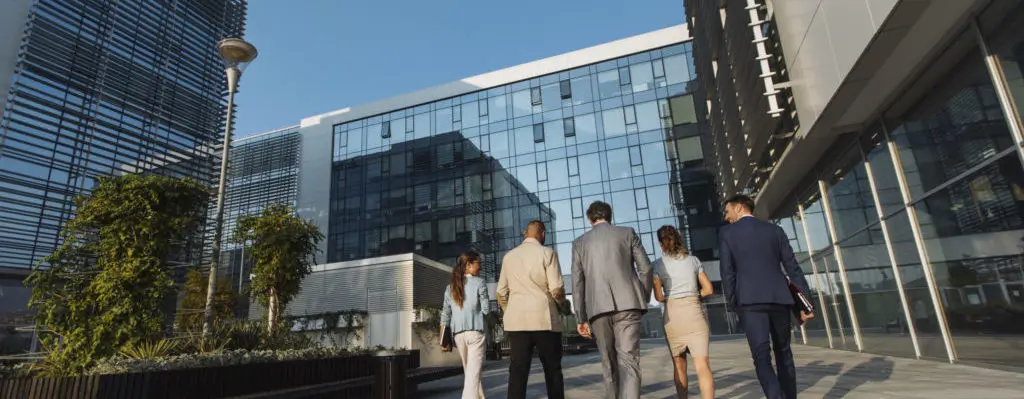 Behind shot of five businesspeople walking next to an office building.