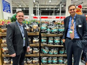 Two men in suits standing in front of a wall of chips inside a store.