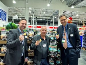 Three men dressed in suits holding potato chips standing in a chip aisle of a store. 