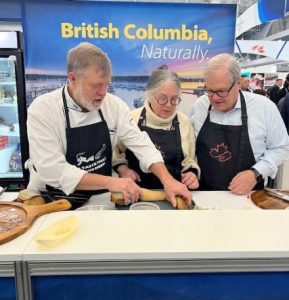 Three people preparing geoduck clam on a table.