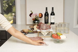 Hand placing an empty wine glass next to two bottles of wine.