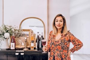 VJ Gandhi holds a glass of wine, standing next to a table of wine, flowers, and a mirror.