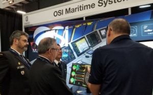 Officers at a trade show listening to an OSI Maritime representative at a booth.