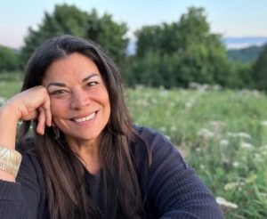 Close-up photo of Patrice Mousseau smiling. Behind her is a green field and trees. 
