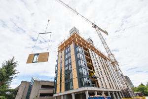 Vista lateral construcción del edificio Brock Commons con grúa levantando gran pieza de madera