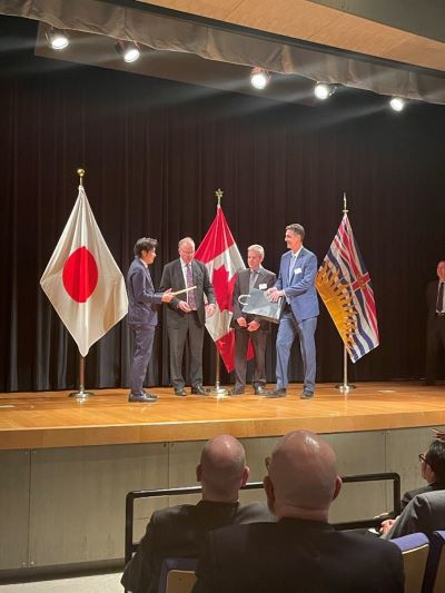 Four people on stage shaking hands next to the Japan, Canada, and BC flag.
