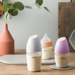 Three kinds of baby bottles with different colour bottle tops displayed on a table.