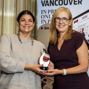 Two women standing and smiling while holding an award together.