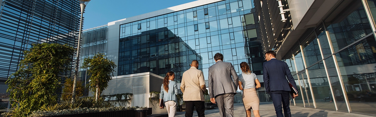 Behind shot of five businesspeople walking next to an office building.