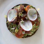 A tostada featuring locally sourced cherry tomatoes, radishes, and herbs with green sauce on a white plate; highlights BC’s agri-food sector potential.